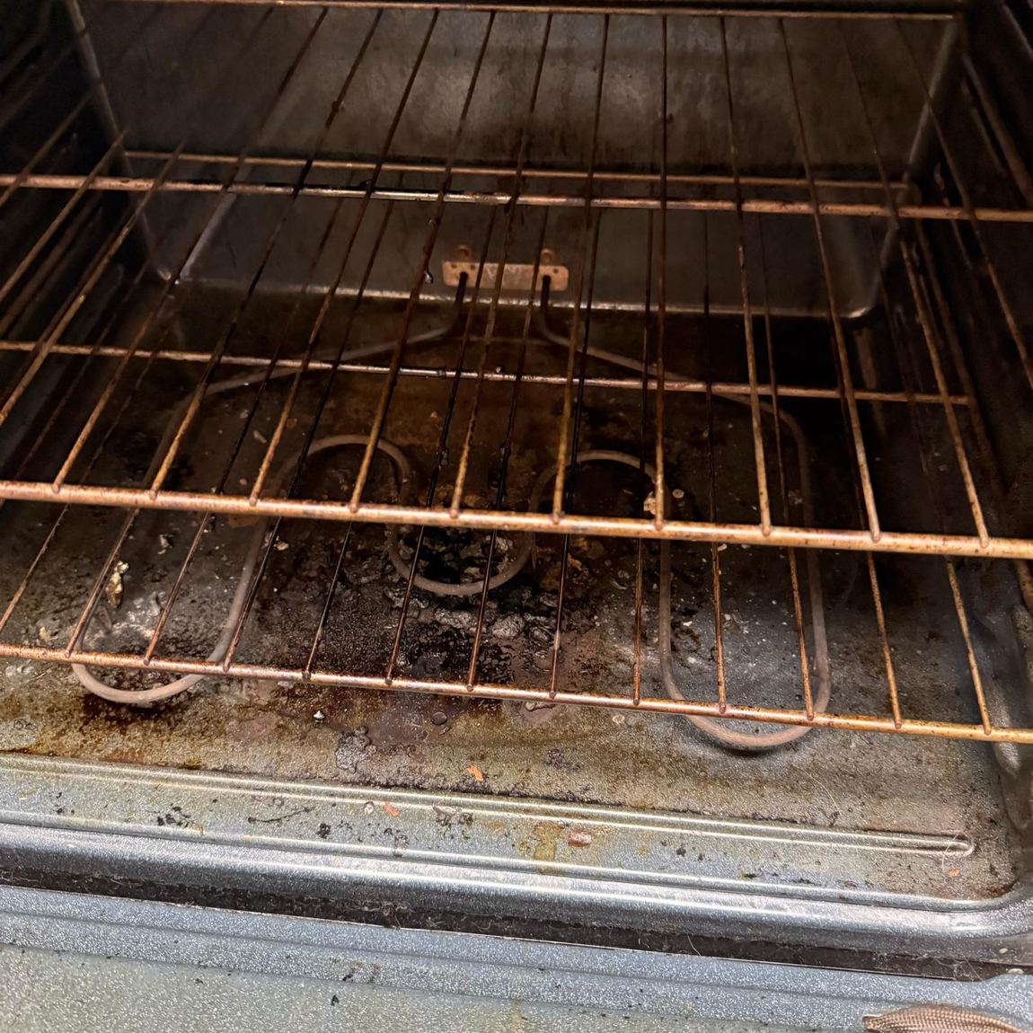 Oven interior before cleaning, with baked-on spills on the racks and floor