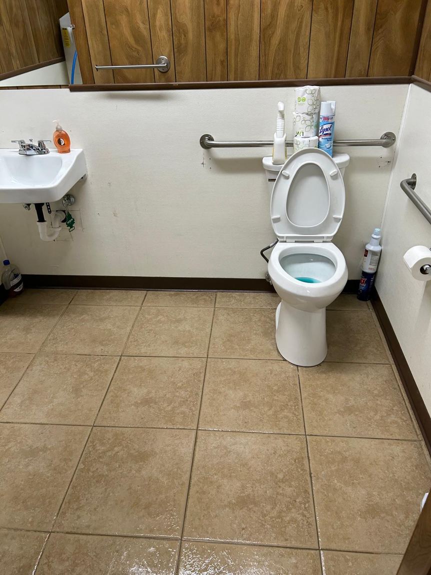 A clean office restroom with sink, toilet, and mopped tile floor